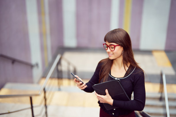 年轻的白人女商人站在地铁的楼梯上，微笑着看着智能手机图片下载