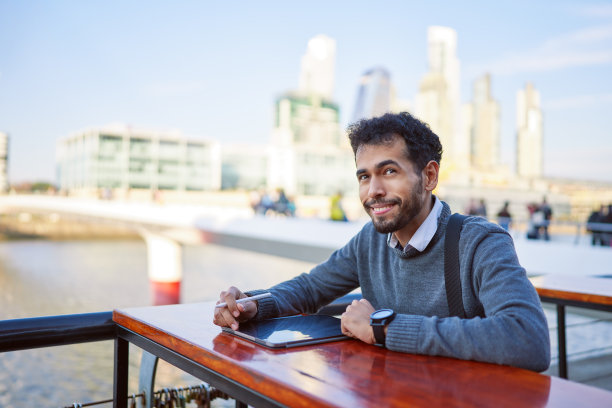 拉丁美洲的年轻人坐在户外拿着平板电脑微笑着工作图片下载