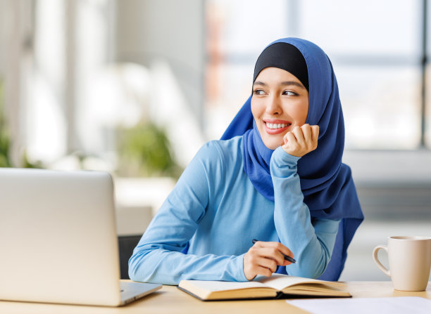 戴着传统宗教头巾的美丽微笑的穆斯林妇女在家里用笔记本电脑远程工作图片下载