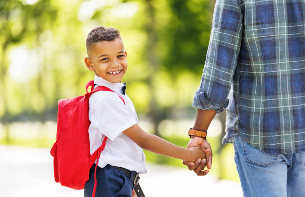在一个阳光明媚的秋日里，一个男生和爸爸一起去上小学一年级，他微笑着看着镜头图片下载