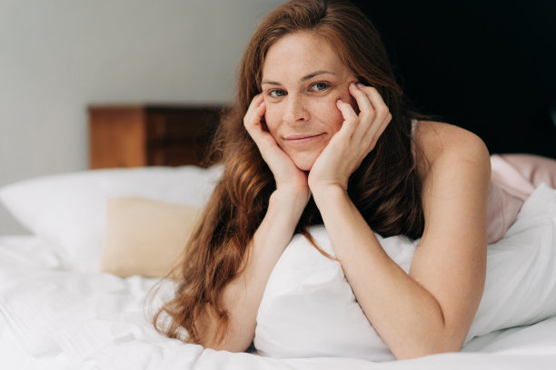 一个年轻漂亮的长发女子，双手抱着头躺在床上。图片下载