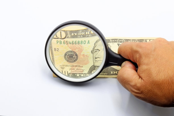 一只手拿着放大镜在检查一张10美元的钞票图片下载