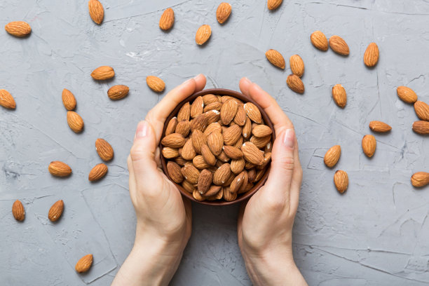 女人手里拿着一个装着杏仁的木碗。健康食品和零食。各种坚果的素食小吃图片下载