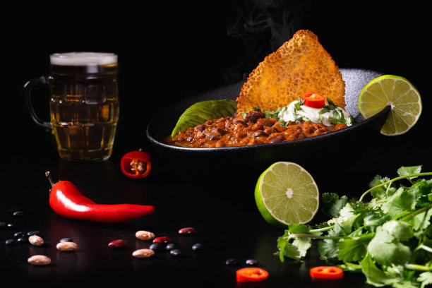 一碗素食辣椒肉酱和辣椒，切青柠和一杯啤酒在黑色的背景图片下载