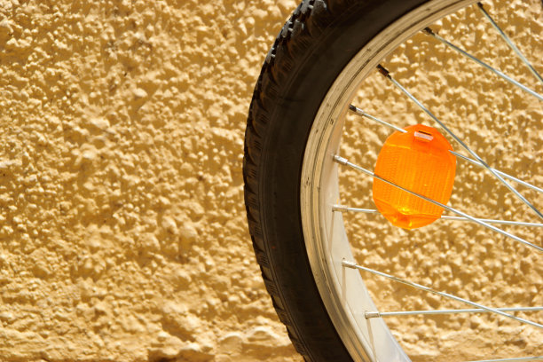 一个明亮的橙色反射镜站在纹理墙的孩子的自行车车轮特写。图片下载