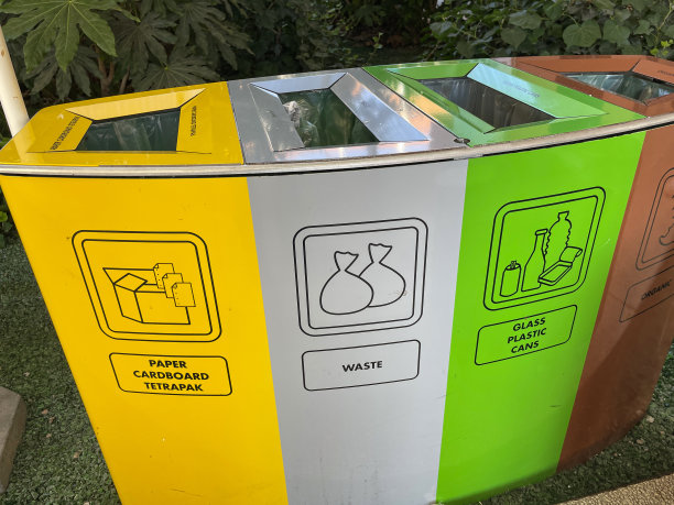 城市街道的特写图片，不锈钢，回收垃圾箱，通过植物边界分开的彩色部分，黄色用于纸张，纸板和利乐包装，绿色用于玻璃，塑料和罐头，棕色用于食物垃圾，银色用于一般垃圾图片下载