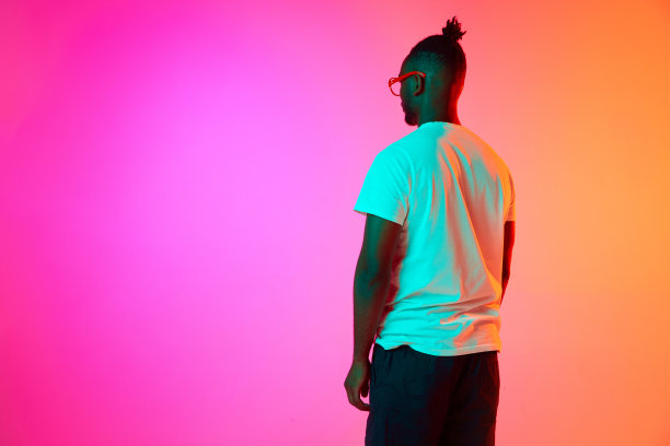 身穿白色t恤的非洲男子在霓虹灯中独自站在橙粉色的背景上。图片下载