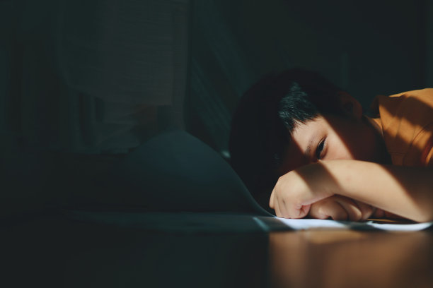 在他家里一个角落的阴影里，一个小亚洲人躺在桌子下面的地板上，用手托着头，看起来悲伤而沮丧。图片下载