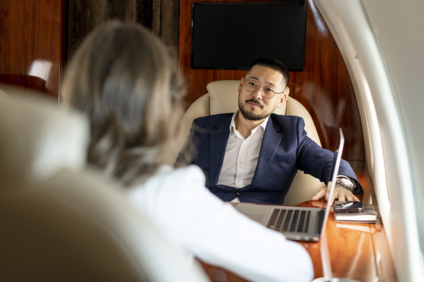 商务人士在私人飞机上讨论交易，西装革履的亚洲商人在飞机上与女同事交谈图片下载