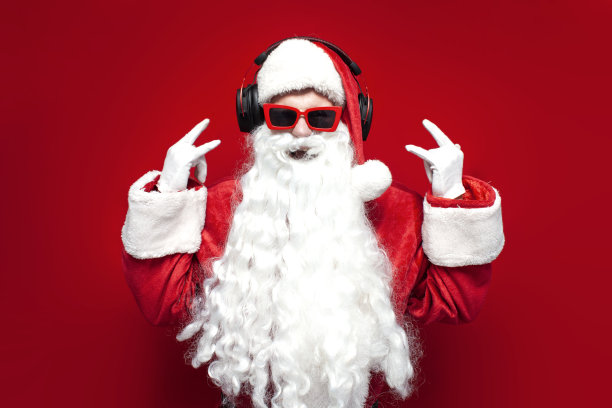 圣诞老人戴着帽子和节日眼镜，用耳机听着音乐，在红色的背景下唱歌图片下载