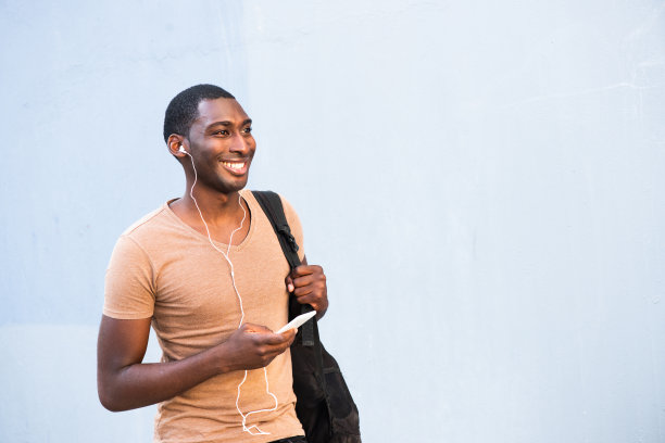 微笑的年轻黑人拿着手机，戴着耳机听音乐图片下载