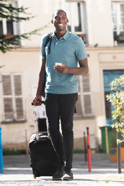 一个全身的黑人年轻人带着行李和手机走在城市街道上图片下载