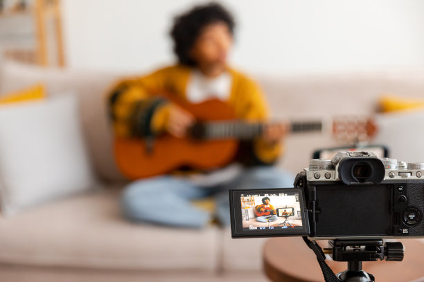 博主吉他手。非裔美国女孩博主弹吉他，对着摄像头录视频。社交媒体影响者女性在家室内流媒体。音乐内容创作者广播教程。图片下载