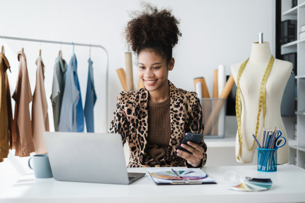 女性时装设计师使用智能手机和带有数字平板电脑的笔记本电脑来获取客户的订单。图片下载