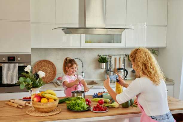 母亲在家里厨房准备食物时用手机给女儿拍照图片下载