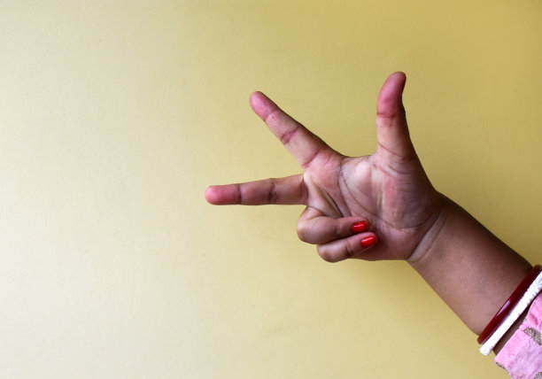 一个印度女人的手特写，在干净的背景上显示出三个手指的手语。图片下载