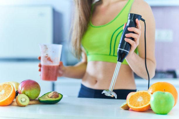 穿着运动服的健身女士在家厨房用手动搅拌器准备新鲜水果奶昔。健康生活方式维他命饮料图片下载