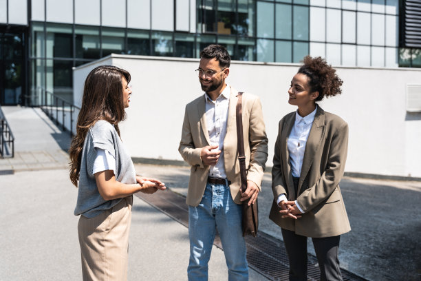 一群商务人士在办公楼前与同事闲聊。年轻的雇员在工作之余闲聊老板图片下载