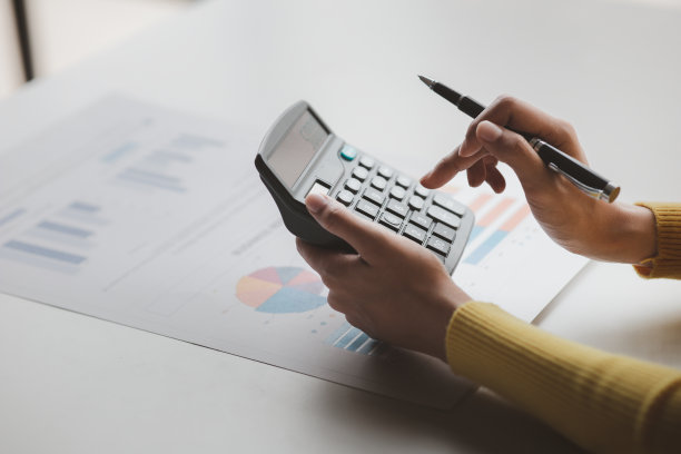 商人用计算器计算公司财务文件上的数字，她正在分析历史财务数据，以计划如何发展公司。金融的概念。图片下载