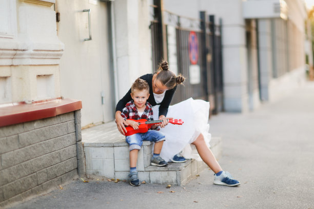 可爱的欧洲年轻母亲和她的儿子在走廊上玩红色的尤克里里。在城里四处走走，学习演奏乐器图片下载