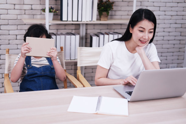 微笑的亚洲母亲和小女孩在客厅里用平板电脑和笔记本电脑一起学习。以科技为理念的家庭教育。图片下载