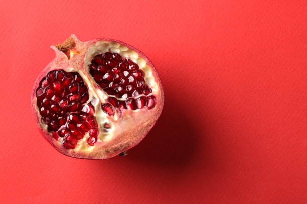 在鲜红的纸背景上切开成熟美味的红石榴果。前视图。文本空间图片下载