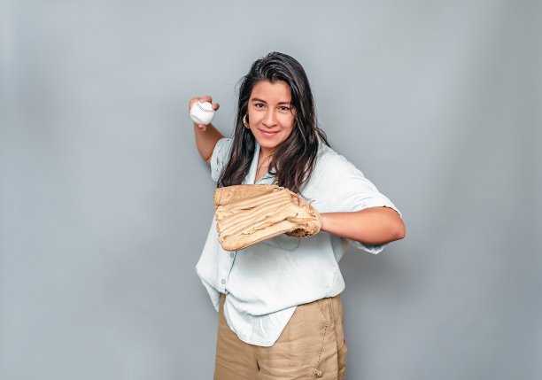 戴着棒球手套的拉丁美洲妇女在扔棒球。一个穿白衬衫和米色裤子的黑发女人。图片下载