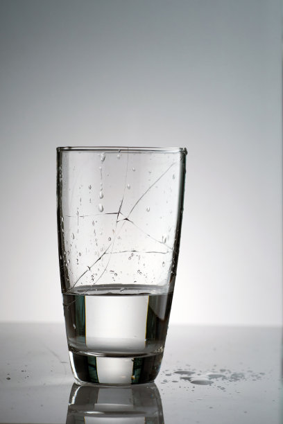 一个装满水的碎玻璃杯和许多飞溅和液滴在桌子表面和背光下图片下载