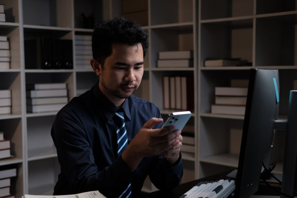 亚洲商人晚上在办公室加班时使用智能手机。图片下载