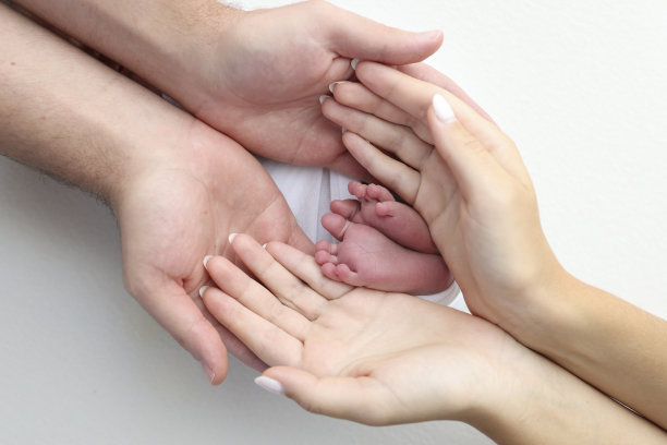 父亲的手掌，母亲的脚都抱着刚出生的婴儿在白色的背景。新生儿的脚放在父母的手掌上。孩子的脚趾、脚后跟和脚的照片。图片下载