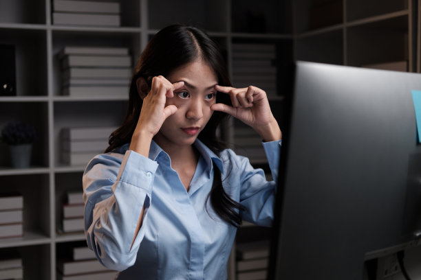 疲惫的年轻亚洲女商人试图在晚上加班的同时保持清醒。图片下载