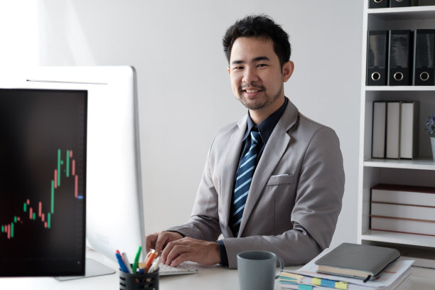 中年亚洲商人分析投资趋势，在办公室的电脑前工作。图片下载
