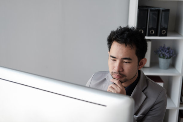 中年亚洲商人分析投资趋势，在办公室的电脑前工作。图片下载