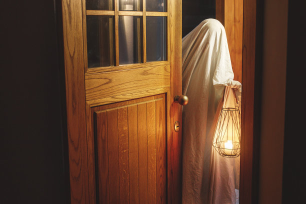 万圣节快乐!不给糖就捣蛋!阴森的幽灵在黑暗中拿着发光的灯笼站在门口。恐怖大气的万圣节时间，人打扮成鬼不给糖就捣蛋。图片下载