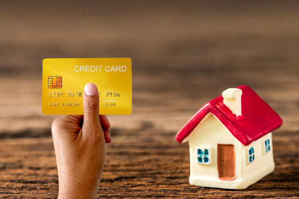 手持演示信用卡和木材背景的房子模型，网上购物的概念图片下载