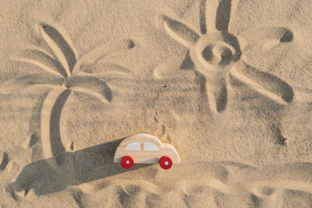 木制玩具车在沙滩背景与画太阳和棕榈。环保出行，减少碳足迹，对环境的影响，有意识的旅行者，环保的，负责任的旅行者生态汽车概念世界无车日图片下载