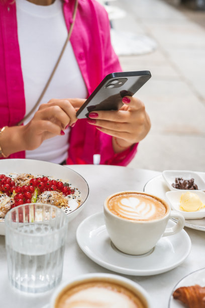 在咖啡馆吃早餐、玩智能手机的女人图片下载