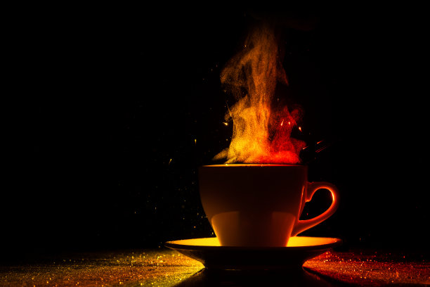 杯子里盛着温热的饮料，袅袅升起的蒸汽，在黑底的红黄橙中闪耀图片下载