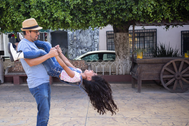 西班牙父亲和女儿在夏天的公园里微笑着玩耍，父亲抱着他的女儿在公园里玩耍图片下载