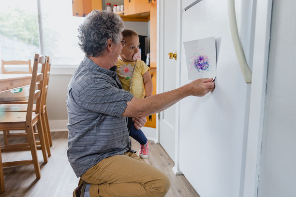 爷爷和孙女把学前班的艺术品贴在冰箱上图片下载