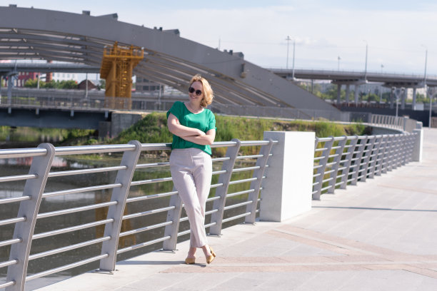 一个女孩的全身画像，穿着衬衫，裤子和太阳镜，背景是未完成的建筑。图片下载