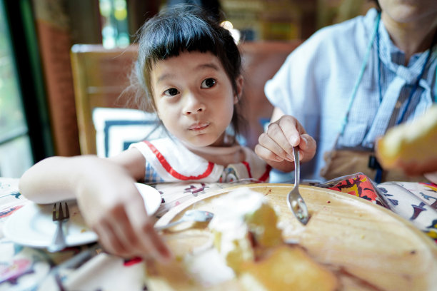 小女孩在餐厅和妈妈一起吃甜点，她的脸很清新，看起来很好吃。开心饭，家庭时光。图片下载