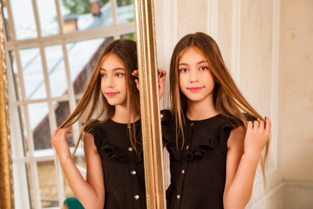 可爱的9-10岁女孩的肖像在客厅的镜子前摆姿势，微笑着看着相机。时尚的儿童模特穿着时尚的黑色连衣裙。时尚青春的风格理念。复制广告文本空间图片下载