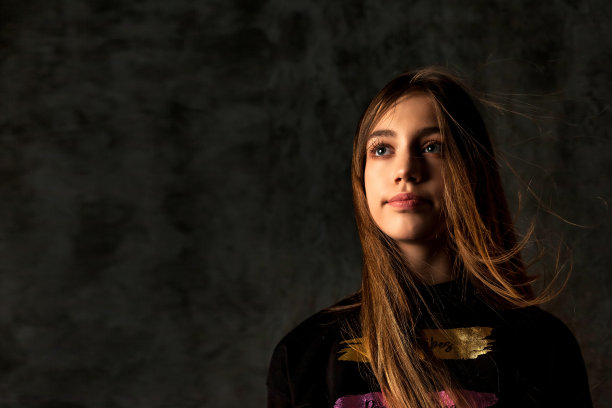封面上的小女孩长发随风在黑暗纹理的墙壁上摆姿势，把目光移开。漂亮的孩子模型9-10岁冻结的眼睛在阴影中摆姿势。表演行为概念。复制广告文本空间图片下载