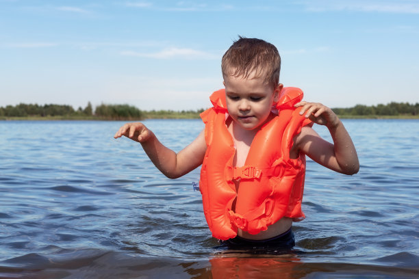穿着橙色游泳背心的小男孩在湖水里的肖像，夏天的假期。图片下载