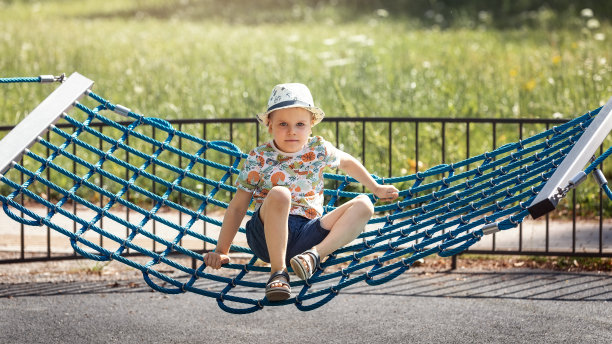 一个微笑的小男孩坐在夏日公园的吊床上摇摆，摆姿势给摄影师拍照图片下载