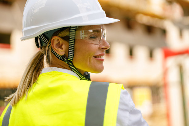 微笑的女建筑工人戴着防护头盔站在建筑背景图片下载