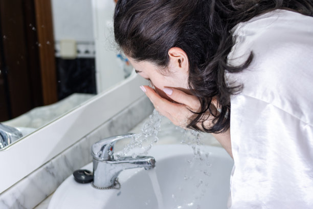 一个女人在浴室的水池边洗脸。早上洗脸的人。图片下载