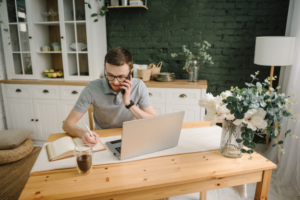 在笔记本上写字。认真的人工作，学习在线笔记本电脑在家庭办公室。交易cryptocurrency。交易员在电话中交谈，投资者经纪人在分析指数。自由职业者。市场营销。沟通图片下载