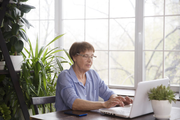 从家里连接互联网的老年妇女。健康的老年人的生活方式。一位在时尚的客厅里使用笔记本电脑在家工作的老妇人。图片下载